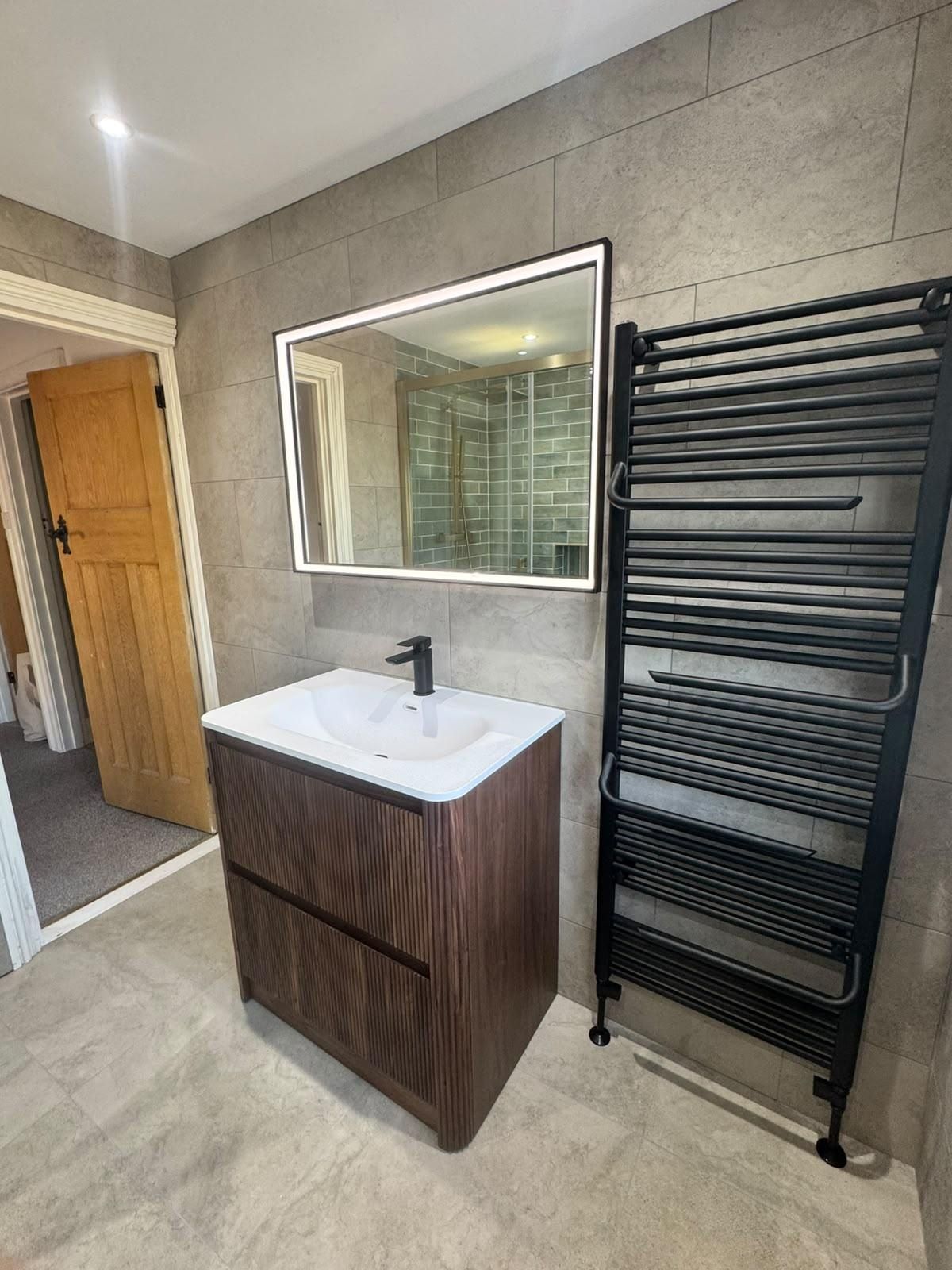 A finished bathroom with a wood vanity unit, LED mirror and black towel radiator