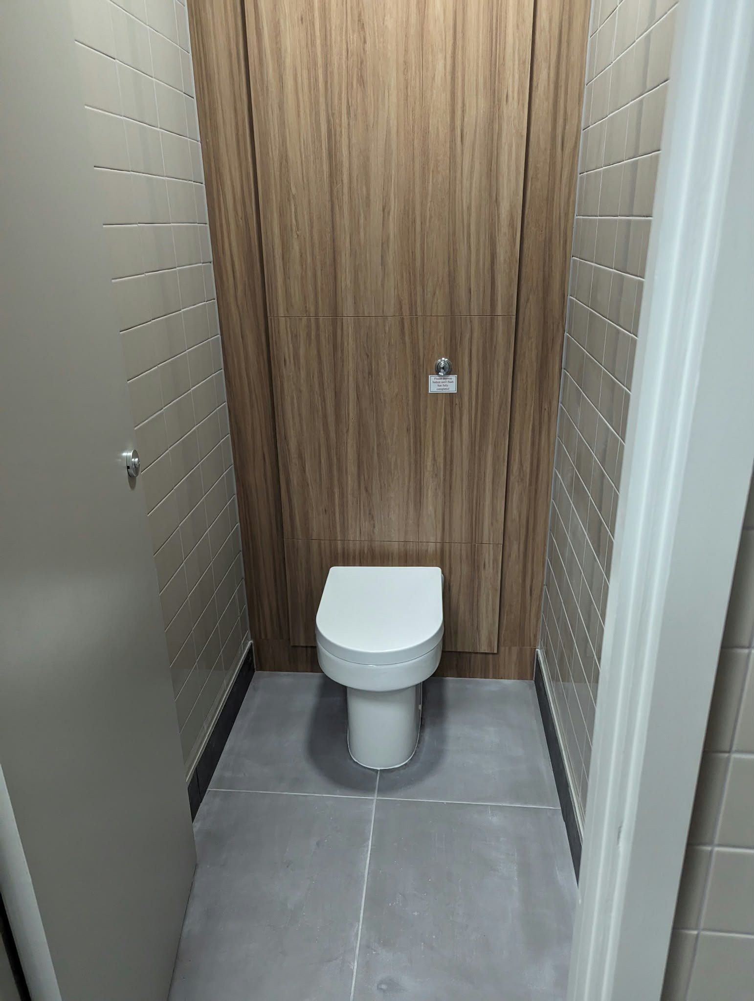 A commercial washroom cubicle with a wood-effect panel and wall-hung toilet