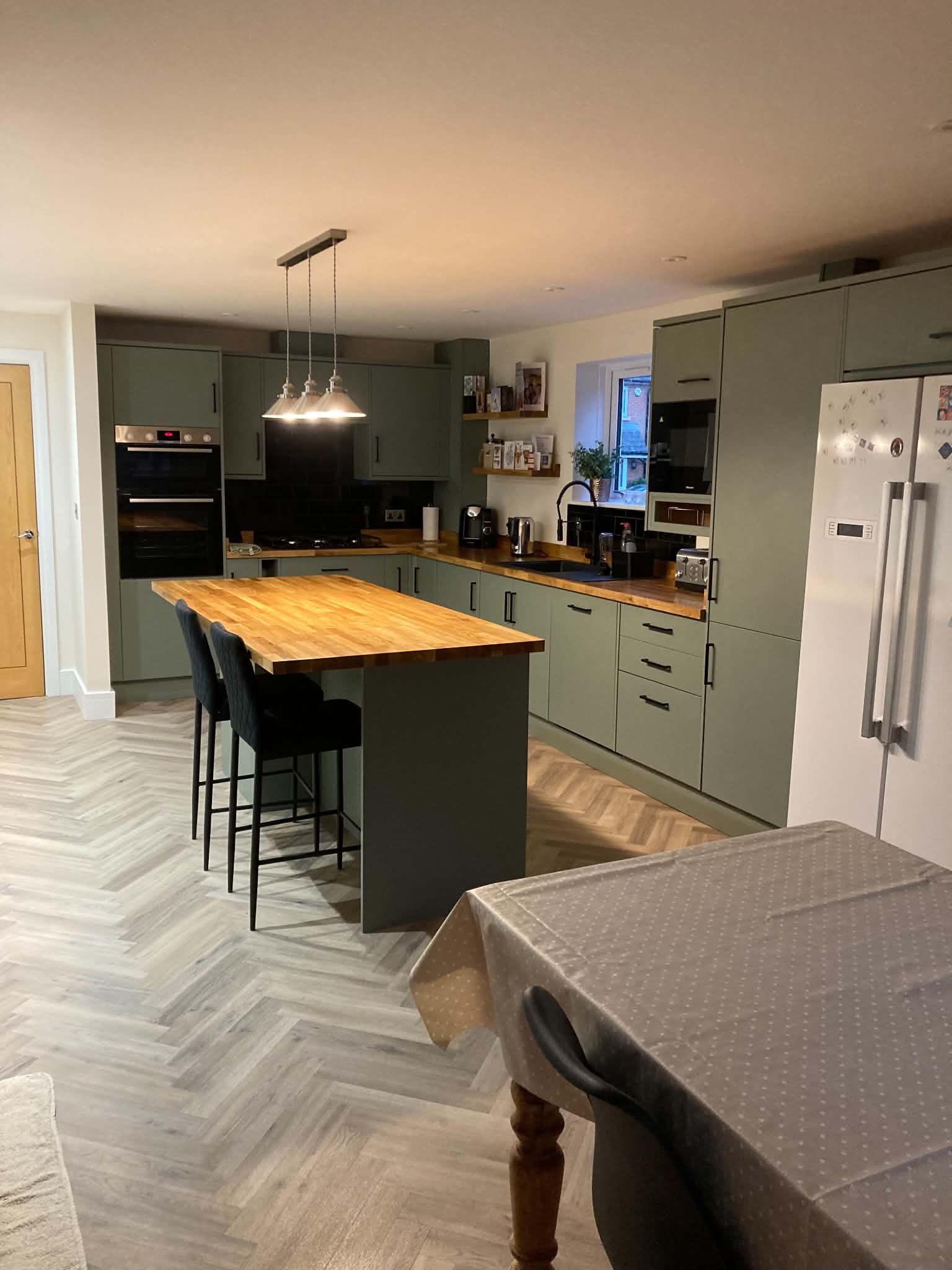 A sage green kitchen island with bar stools, next to the dining table