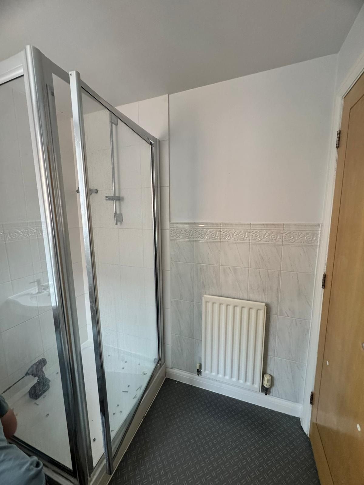 Before: a dated white shower enclosure, tiled splashback and radiator