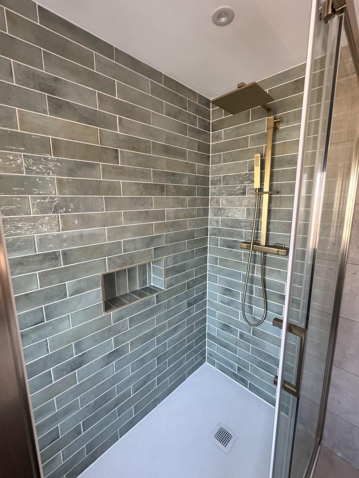 Close-up of green tiles, a built-in niche and brushed brass shower fittings