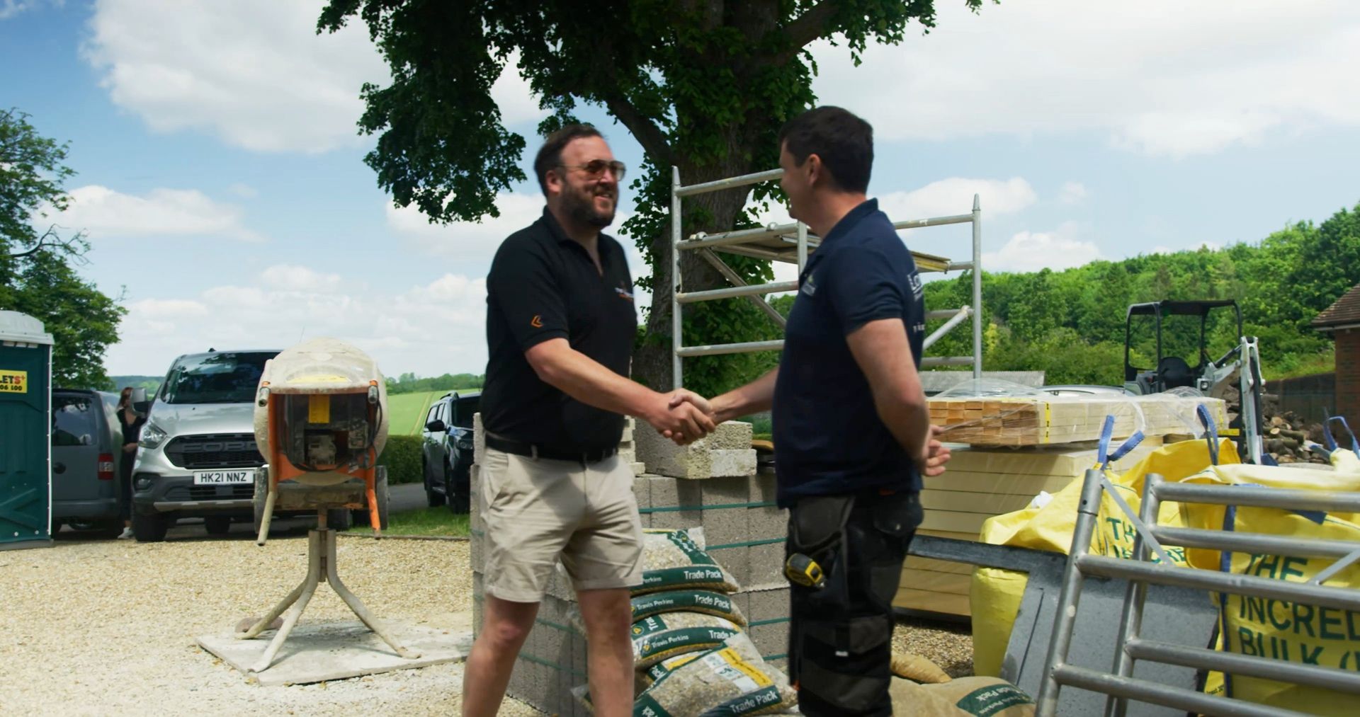 A Kaye Co team member shaking hands with a builder on site, next to a delivery of aggregate and blocks