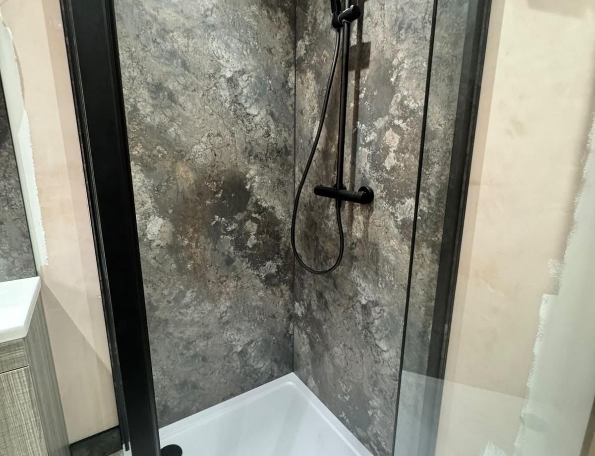 A walk-in shower with dark stone-effect wall panels and a black shower