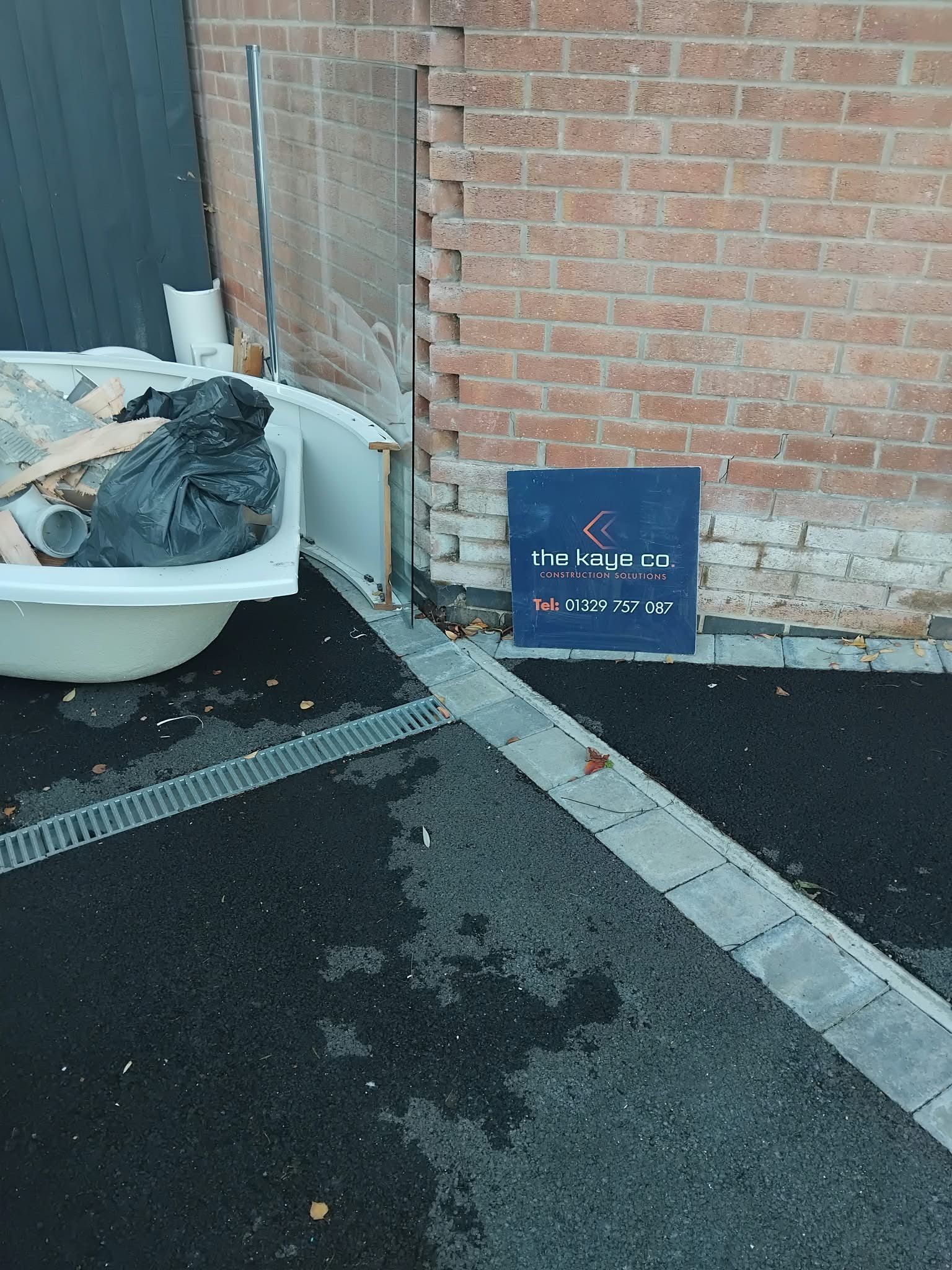 An old bath and rubble outside the house, next to a Kaye Co sign