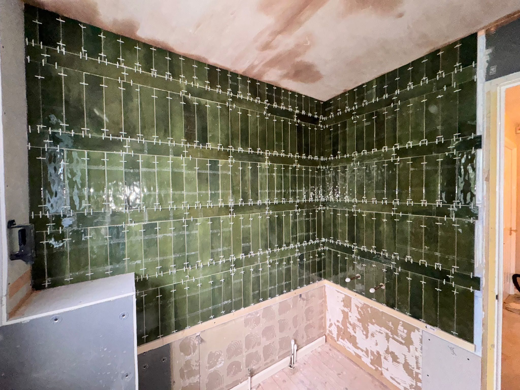 Two walls of green gloss tiles finished, with the levelling clips still in