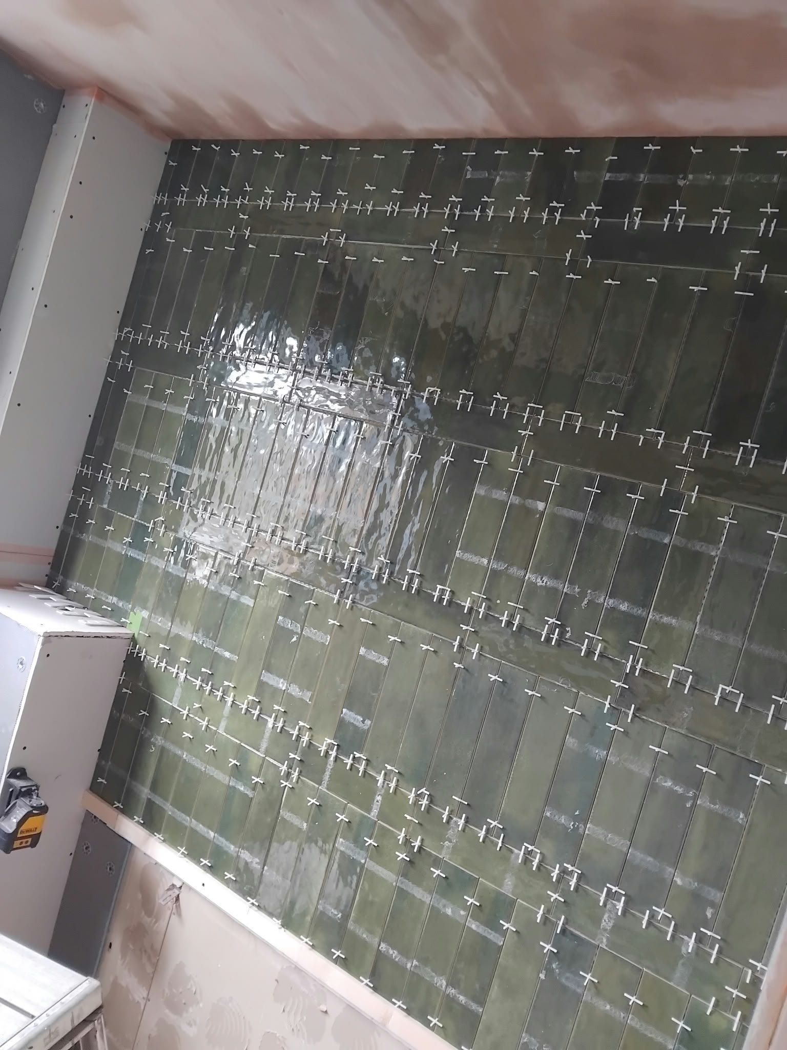 Green gloss tiles going up on a bathroom wall, with levelling clips still in place